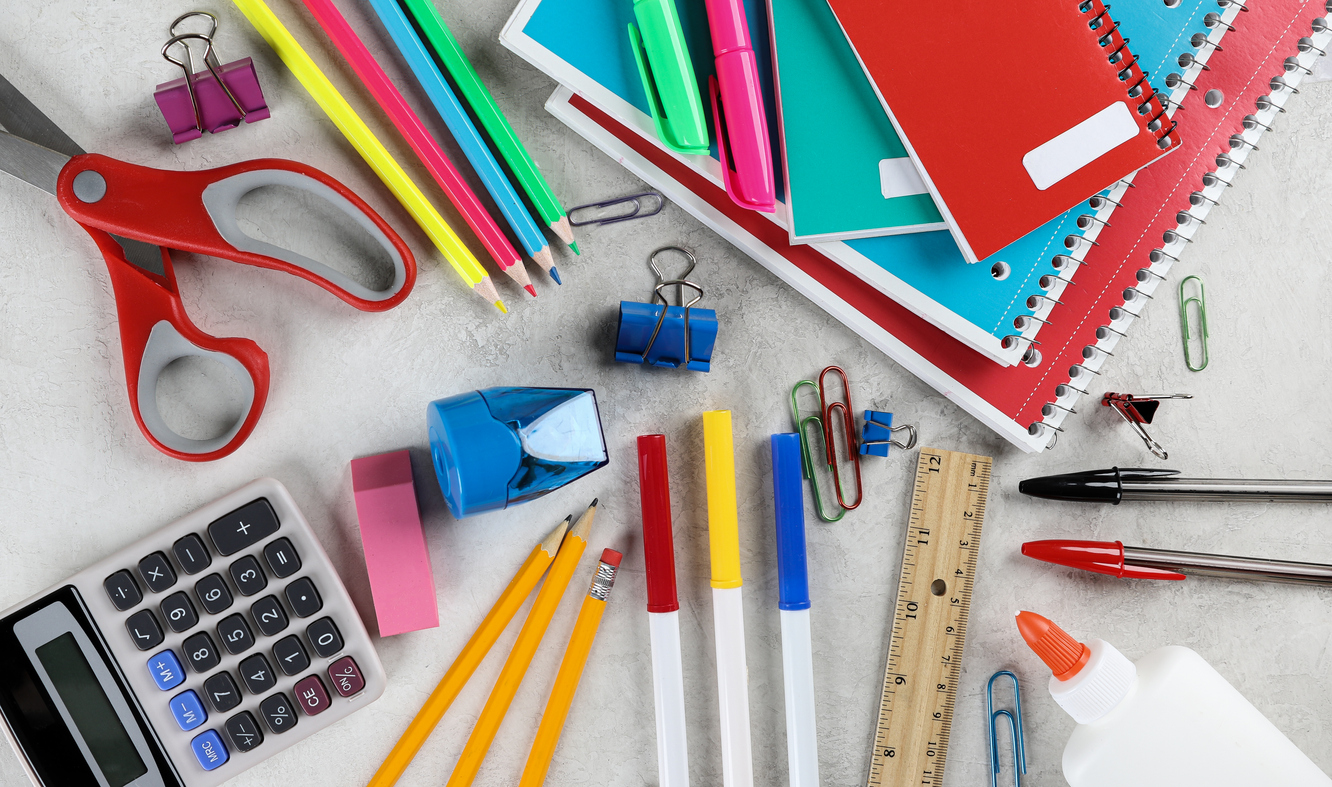 A variety of colorful school supplies spread out on a table, including pencils, pens, notebooks, a calculator, scissors, and glue.