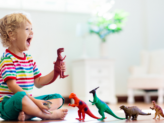 A joyful young child playing with colorful dinosaur toys in a bright, airy room, laughing gleefully while sitting on the floor.