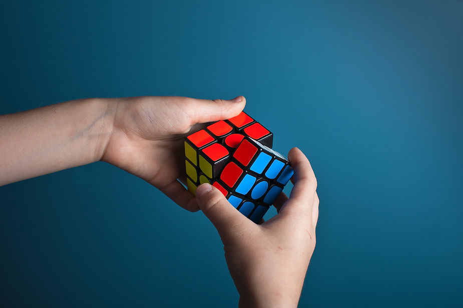Two hands holding a partially solved rubik’s cube against a solid blue background.