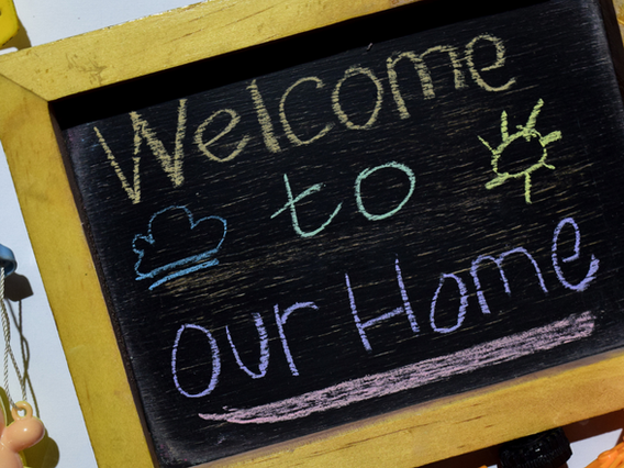 A small chalkboard with the words "welcome to our home" written in white, yellow, and pink chalk, decorated with a chalk-drawn cloud and heart.