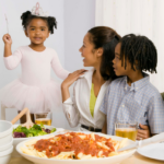 Family sits around a dinner table. They are looking at the little girl who is wearing a tiara.