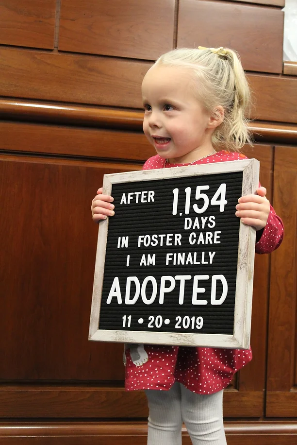 Foster child with sign stating she was adopted after 1154 days in foster care.