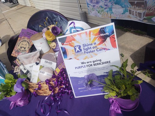 Promotional materials on a table celebrating foster care awareness month, featuring a sign about shining a light on foster care and various purple themed items and decorations.
