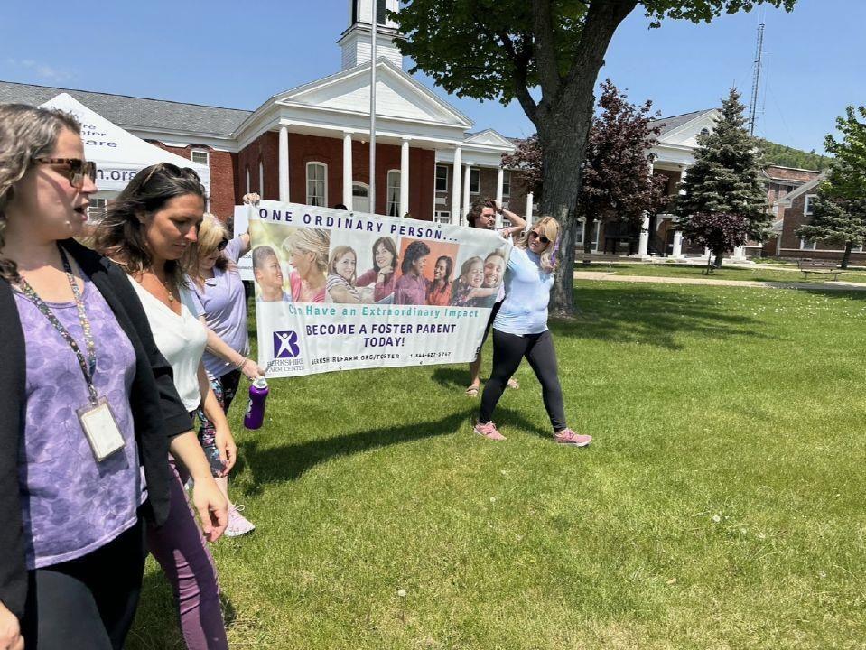 A group of people walking on grass in front of a building. They are holding a banner that reads, 